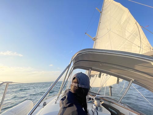 Original iPhone photo of a sailboat on open water — flat contrast, slightly hazy sky, muted blues