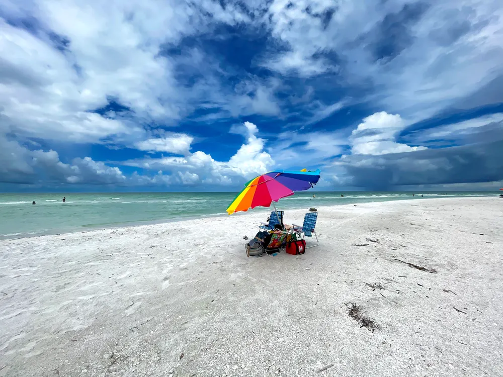 A beach with a rainbow umbrella under a deep blue sky, after the edit